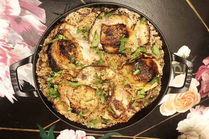 Roasted chicken thighs on a bed of rice with herbs in a Staub cast iron pan, placed on a floral-patterned surface.