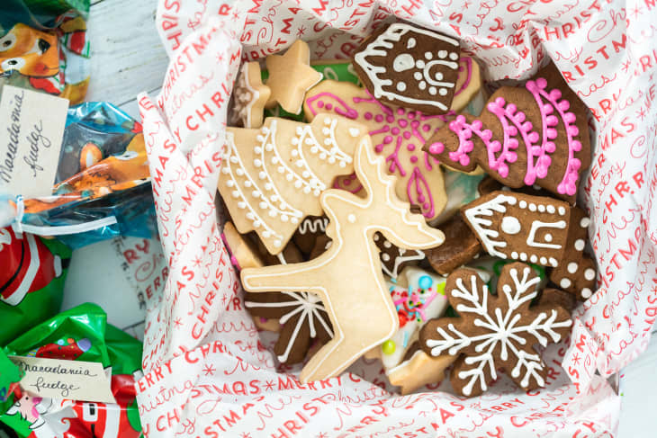 Assorted Christmas cookies with icing in festive wrapping paper, featuring reindeer, snowflakes, and gingerbread houses.