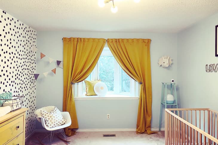 Nursery with yellow curtains, polka dot accent wall, rocking chair, and wooden crib.