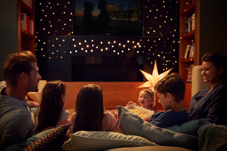 Family watching TV in a cozy living room with string lights, a star lamp, and a bowl of popcorn.