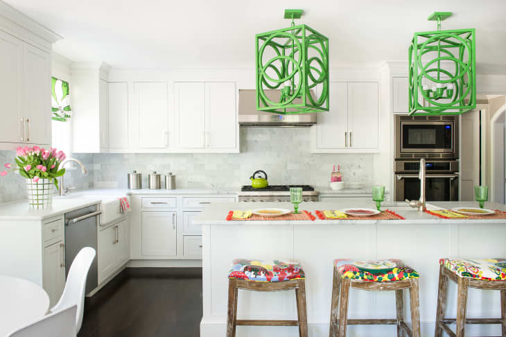 White kitchen with green pendant lights, floral bar stools, pink tulips, and stainless steel appliances.