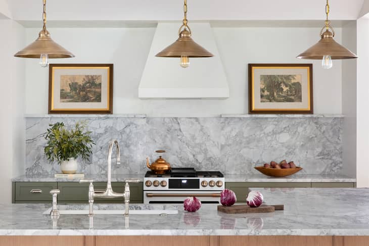 Marble kitchen with brass pendant lights, framed art, and a copper kettle on the stove. Radicchio on the counter.
