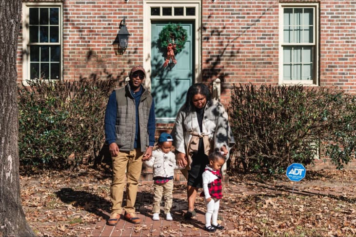 A Black family of four standing in front of a house with a turquoise door. Everyone is dressed in formal clothes, with fall leaves on the ground.