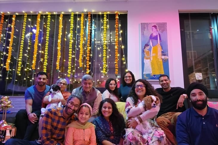 Family gathering in a living room with festive lights and marigold garlands, featuring a painting and two small dogs.