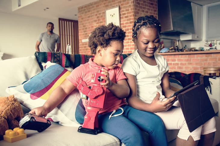 siblings on a couch playing with both ipad games and robots