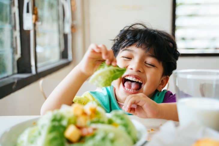 small kid eating salad with a big smile