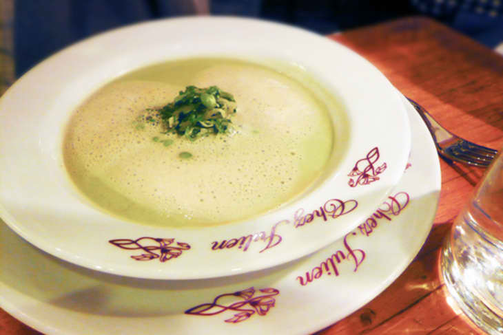Creamy soup garnished with herbs in a white bowl on a wooden table.