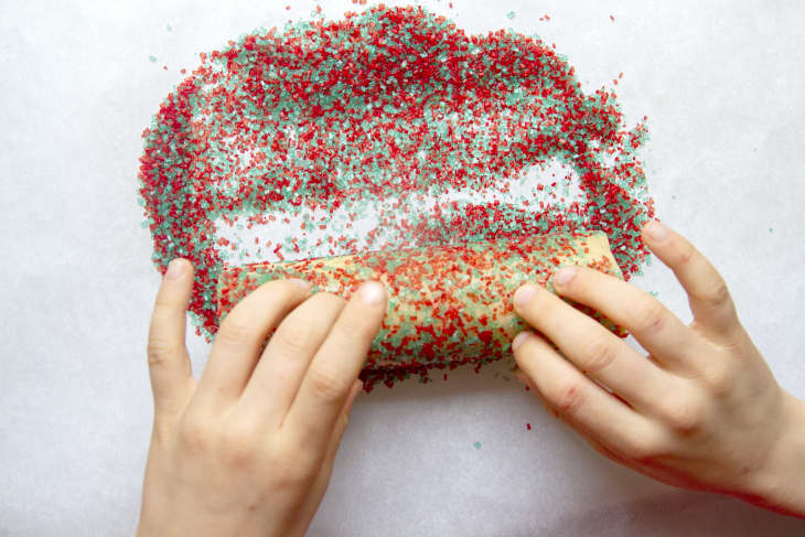 someone rolling dough in sprinkles with their hands