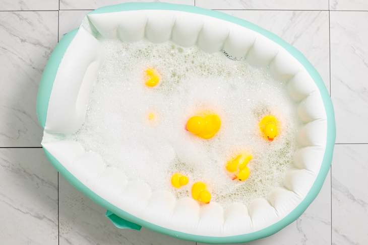 Overhead view of inflatable teal and white baby bathtub filled with water, bubbles and rubber ducks.