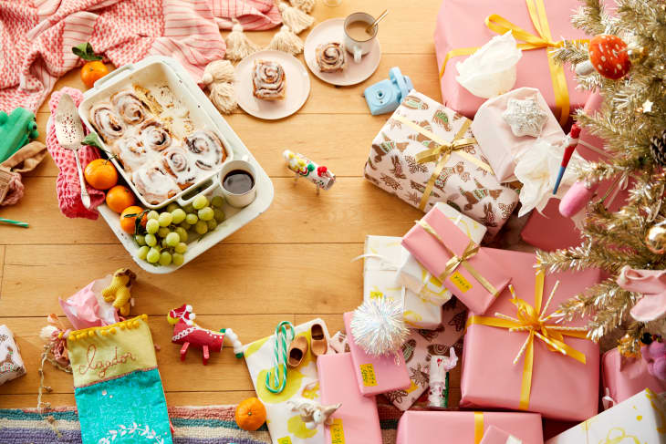 Gifts sit under a christmas tree, while a platter of sweet rolls, fruit, and tea are on the floor ready for Christmas Breakfast.