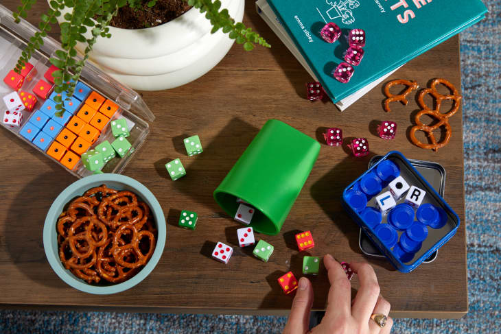 someone holding dice on top of a game with books and pretzels on a table