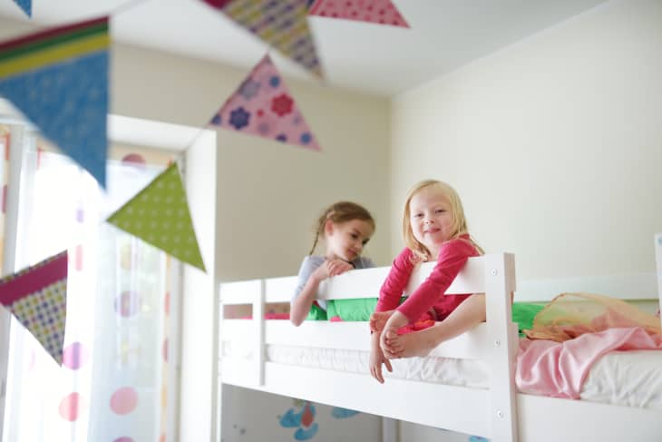 two girls sitting on top bunk of a white bunk bed