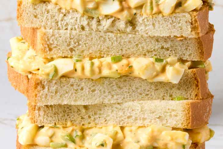 head on shot of four halves of an egg salad sandwich stacked on one another.