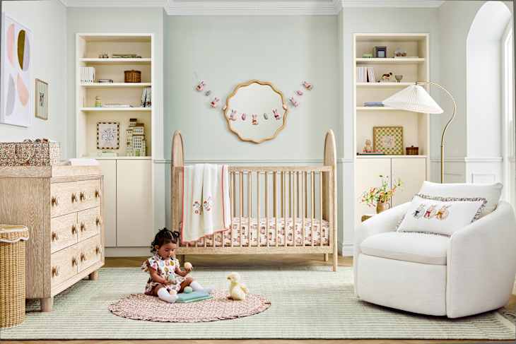 A cozy nursery featuring a wooden crib, a child playing on a round rug, and soft pastel decor.