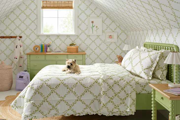 Cozy attic bedroom with green floral bedding, a small dog on the bed, and a light wood dresser.
