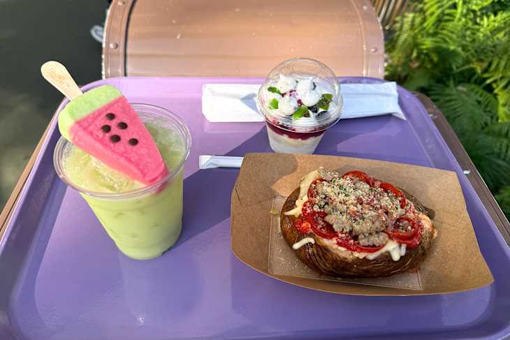 A colorful dessert tray featuring a watermelon-shaped popsicle, a layered parfait with fruit, and a savory pastry topped with pepperoni and cheese.