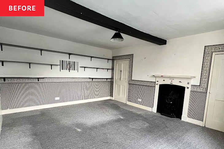 Empty room with gray carpet, patterned wallpaper, black shelves, and a decorative fireplace.