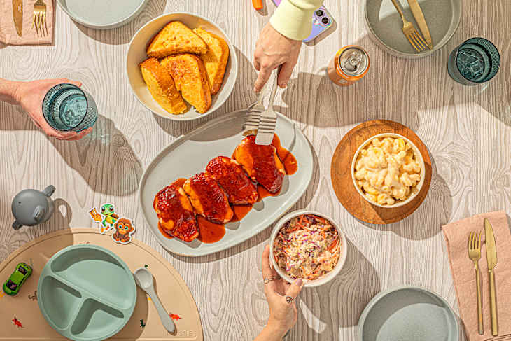 A table set with a meal featuring barbecue chicken, macaroni and cheese, coleslaw, and cornbread, with drinks and utensils.