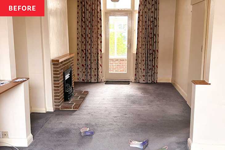 Living room with a brick fireplace, floral curtains, and a gray carpet, featuring scattered children's shoes.