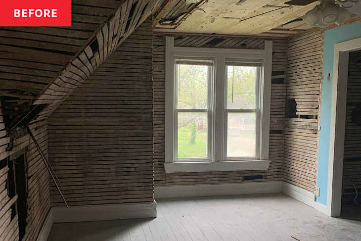 Room with exposed wooden slats on walls, two windows, and a ceiling fan, showing renovation progress.