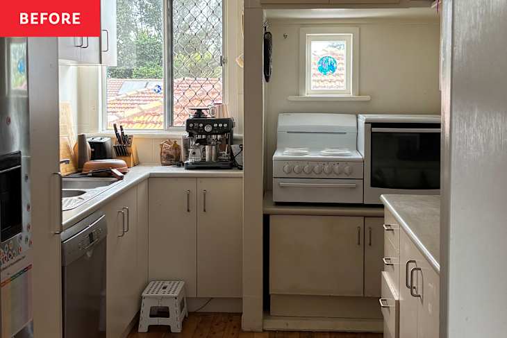 Compact kitchen with white cabinets, a coffee machine, stove, and a window overlooking a tiled roof.