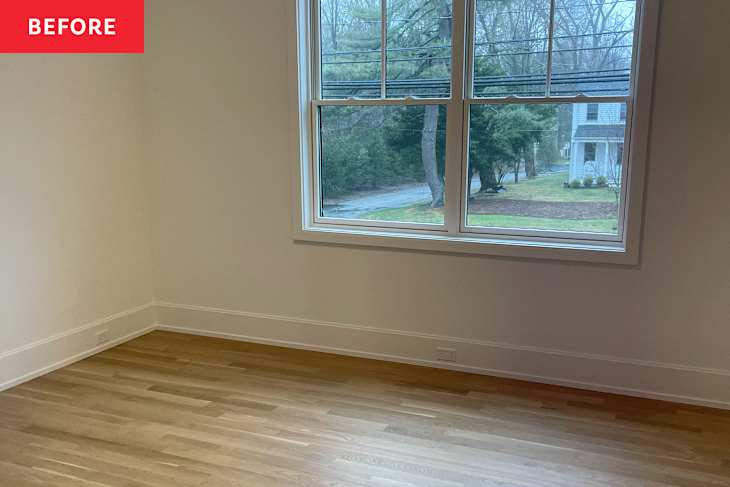 Empty room with light wood flooring, large window showing greenery outside, and neutral-colored walls.