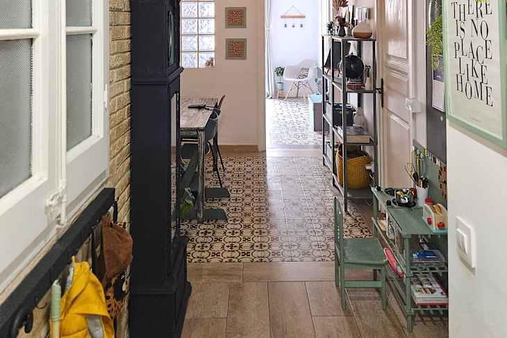 Hallway with patterned tile floor, wooden dining table, green shelving unit, and colorful decor items.