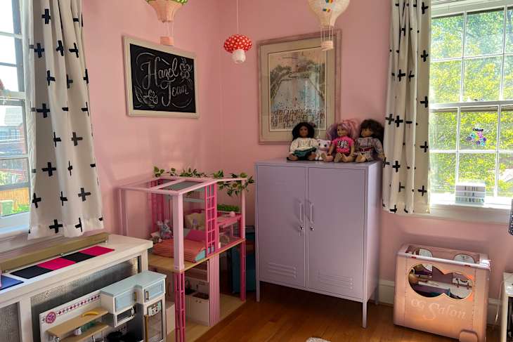 Purple storage cabinet filled with doll accessories, three dolls on top, and a pink salon playset beside it.