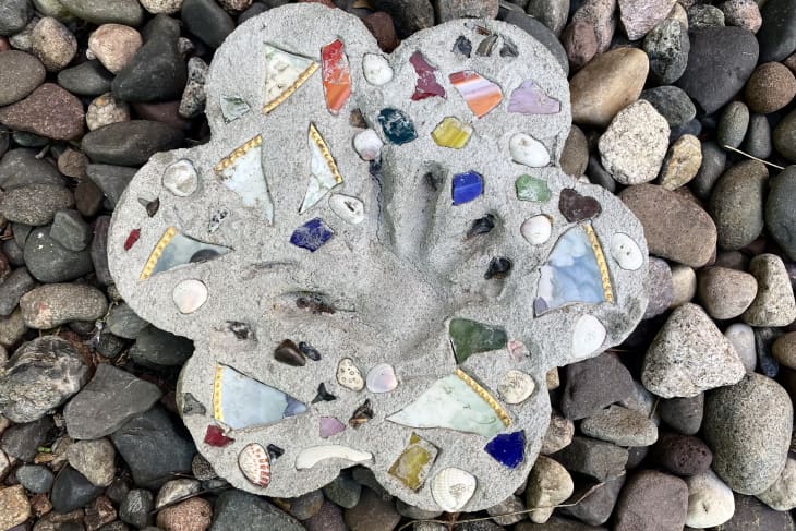 Concrete stepping stone with colorful mosaic tiles and shells on a bed of river rocks.