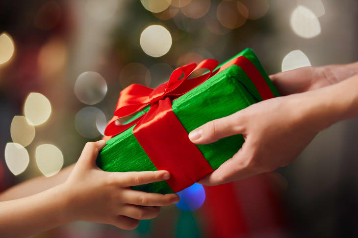 hands around a gift wrapped in green wrapping paper with red bow