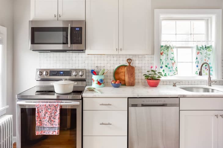 Modern kitchen with stainless steel appliances, floral curtains, a white pot on the stove, and colorful utensils on the counter.