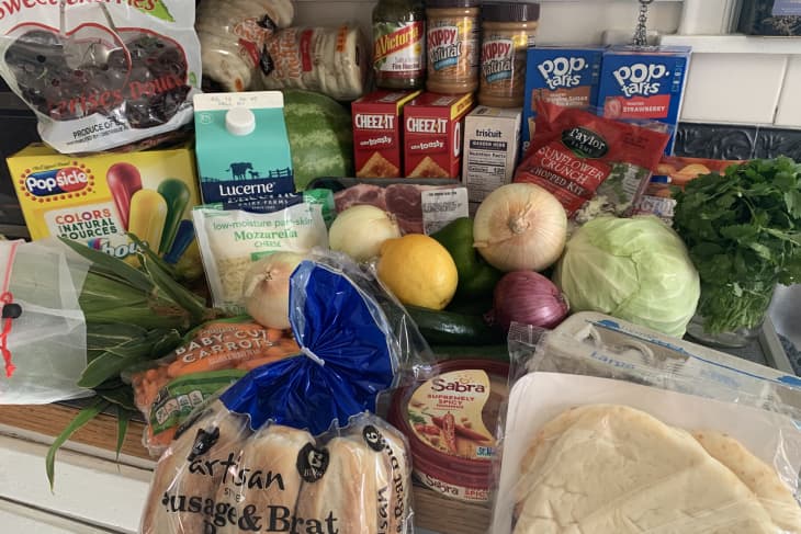Assorted groceries on a counter, including fresh produce, bread, cheese, peanut butter, and packaged snacks.