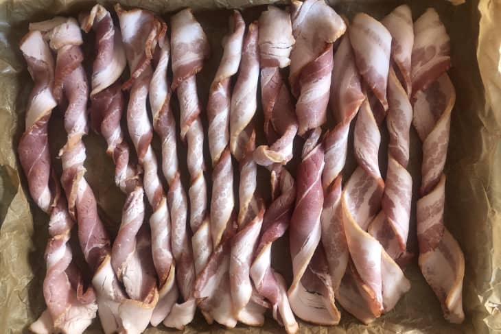 Twisted bacon strips arranged on a parchment-lined baking sheet.