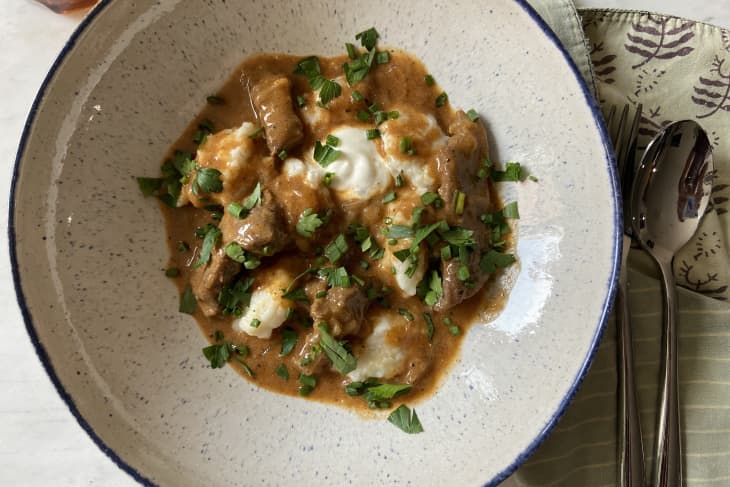 Beef stroganoff with creamy sauce and dumplings, garnished with fresh parsley in a speckled bowl.