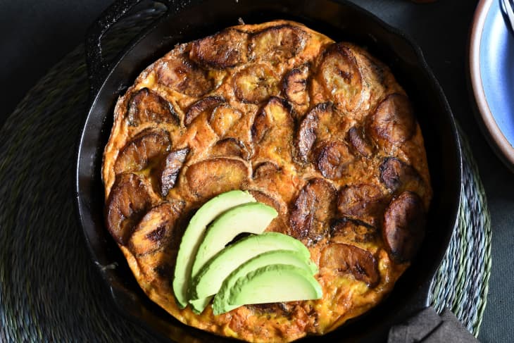 Plantain frittata in skillet with avocado slices on top.