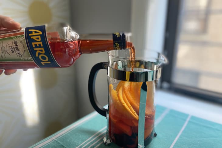 Someone pouring Aperol into a french press to make an Aperol spritz sangria