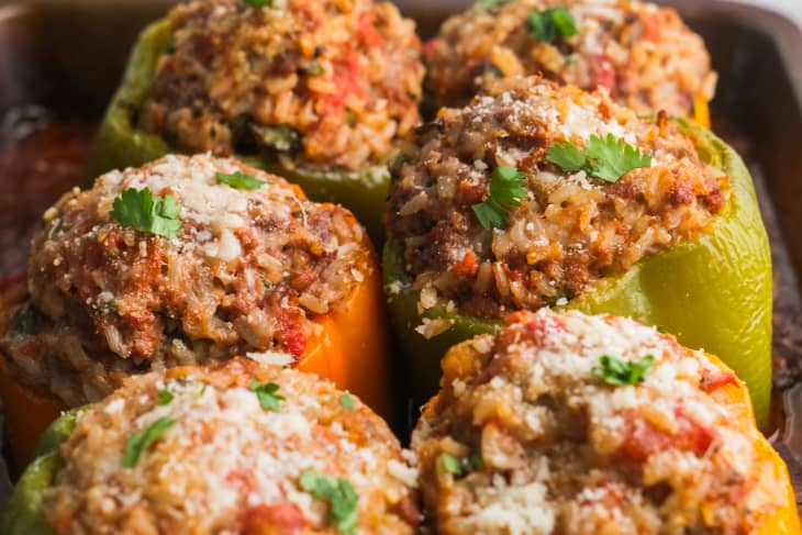 green, orange, and yellow bell peppers stuffed with meat, cheese and herbs on baking sheet