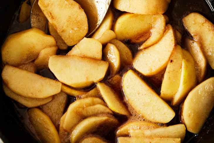 Sliced apples cooked in a spiced syrup, with a shiny glaze and a spoon resting among them.