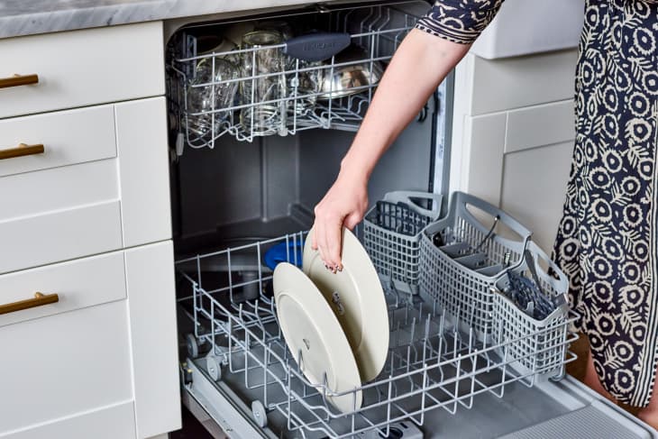 A woman puts a plate in the dishwasher rack