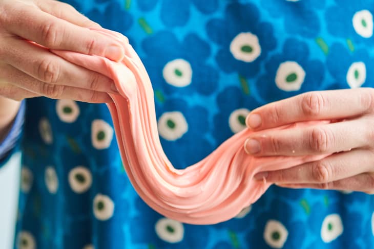 Hands stretching pink slime in front of a blue floral-patterned shirt.