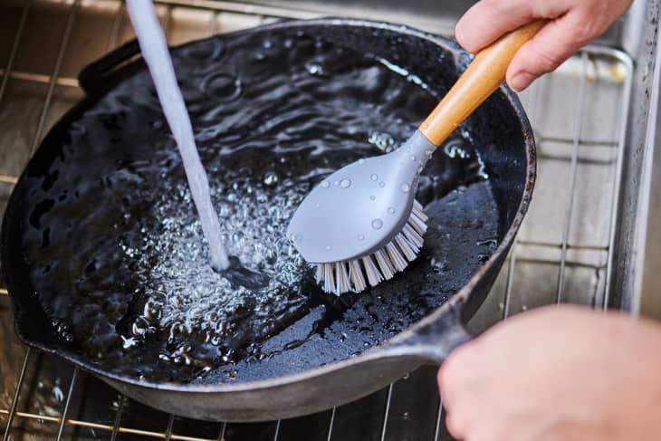 Cleaning a cast iron skillet with a brush in the sink