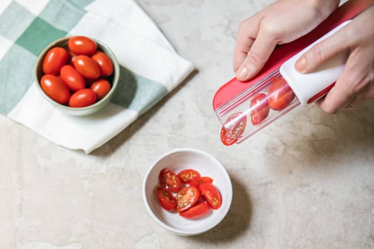 Using a cherry tomato cutting tool to slice cherry tomatoes into a small bowl