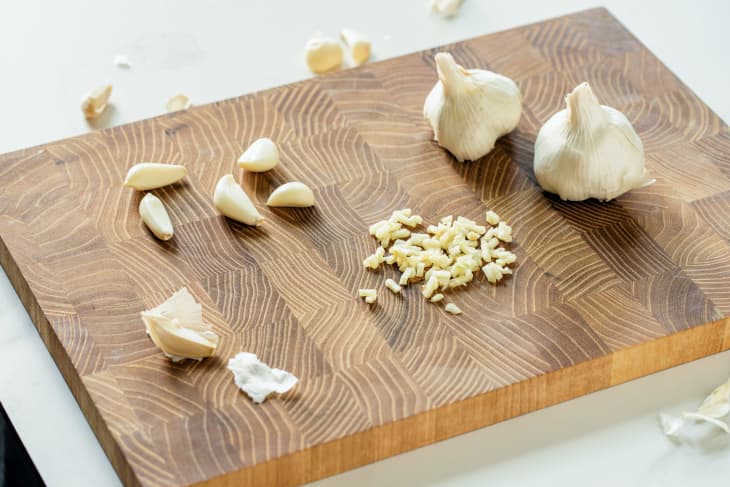 Whole garlic cloves, individual peeled cloves, and a small pile of pressed garlic on a cutting board