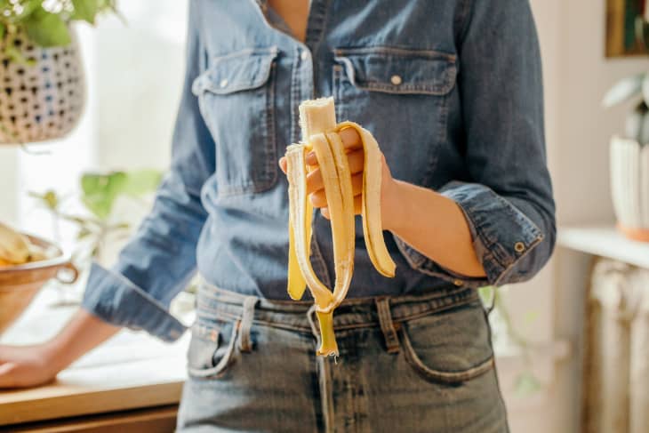 Woman in denim holds a partially eaten/peeled banana.