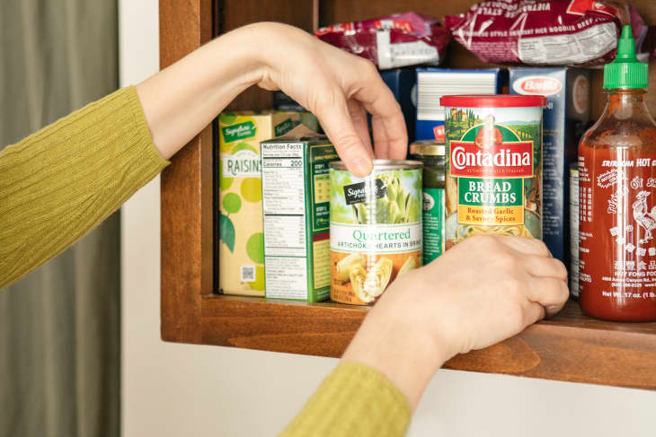 Someone straightening cans in kitchen pantry.