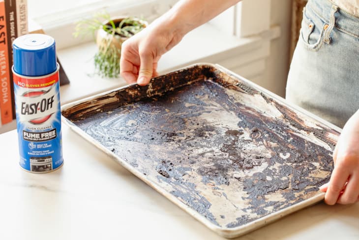 Someone holding dirty baking sheet with can of Easy Off on countertop.