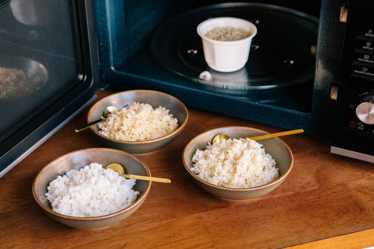Bowls of microwavable rice outside of microwave with open door.