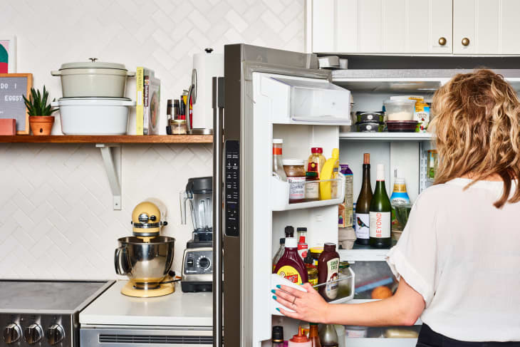 A person standing in front of an open refrigerator inside a kitchen