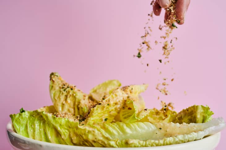 Hand sprinkles breadcrumbs over romaine leaves.