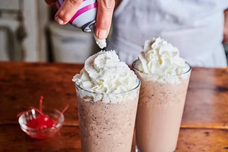 Whip cream is added to the top of a chocolate milkshake.